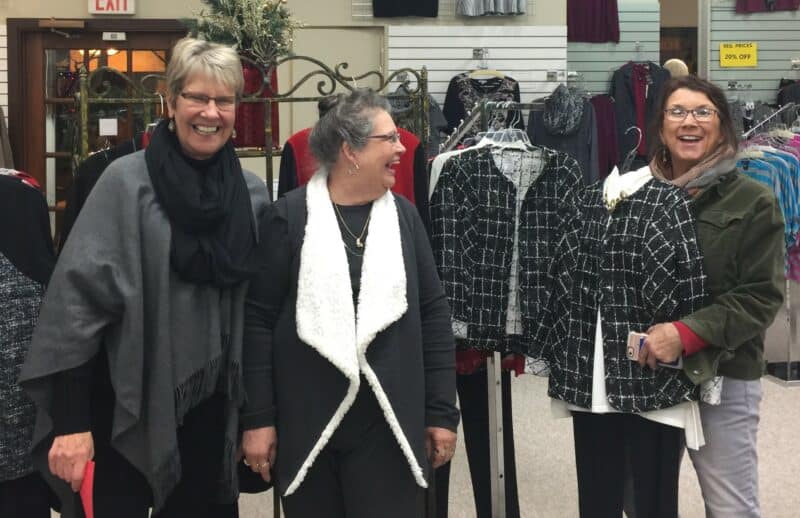 Three happy women stop and smile in a clothing store.